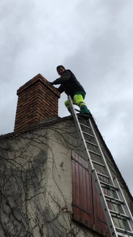 Ramoneur en haut de son échelle, au niveau de la souche de cheminée d'un pavillon