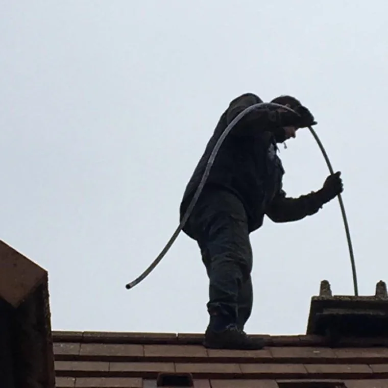 Ramoneur en tenue de travail sur le faîtage d'un toit, canne de ramonage à la main